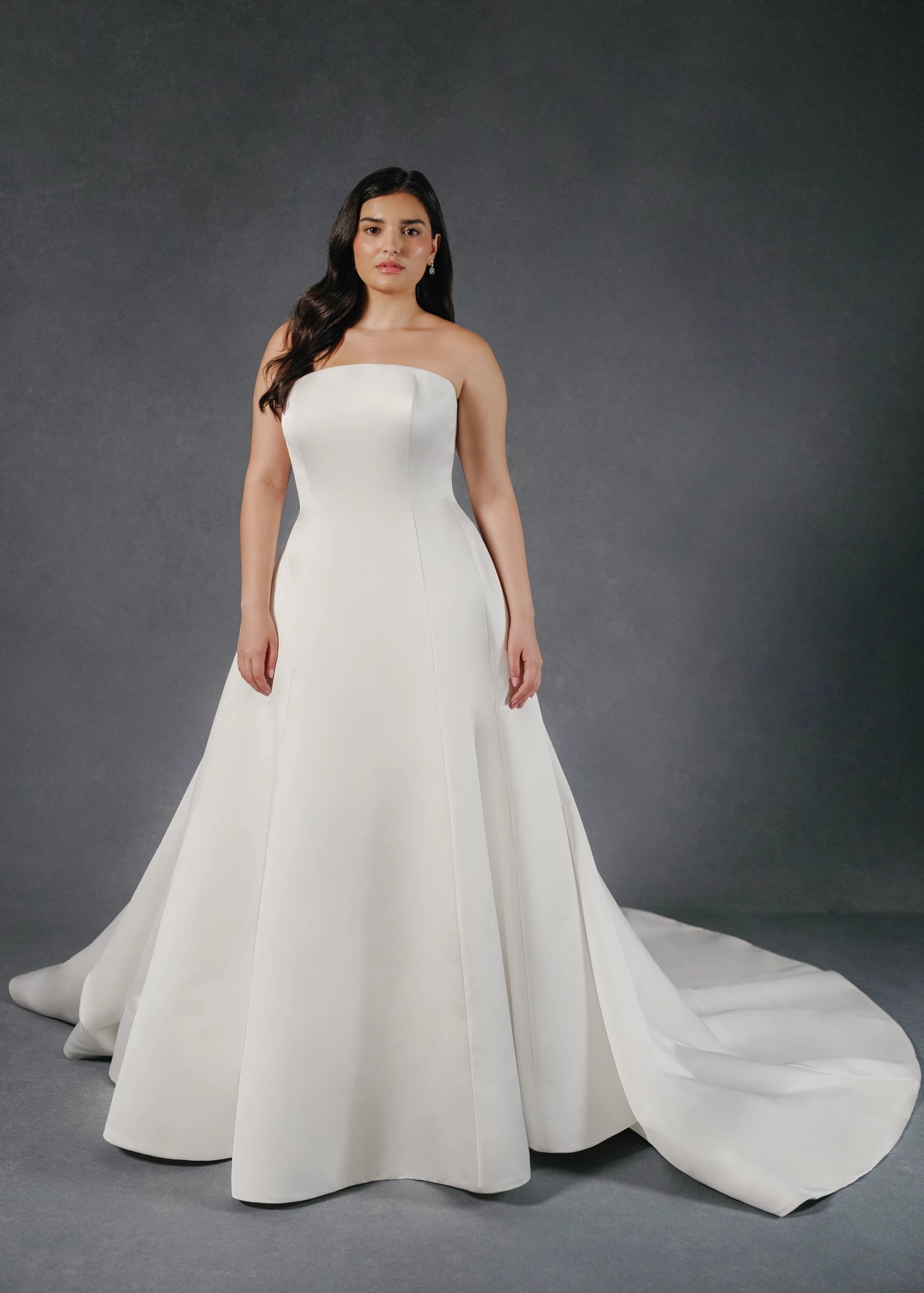 The Loyola gown is an arched strapless A-line gown of Faille-Back Satin with dramatic extended train and buttons to the hem in Silk White and Bright White. 
