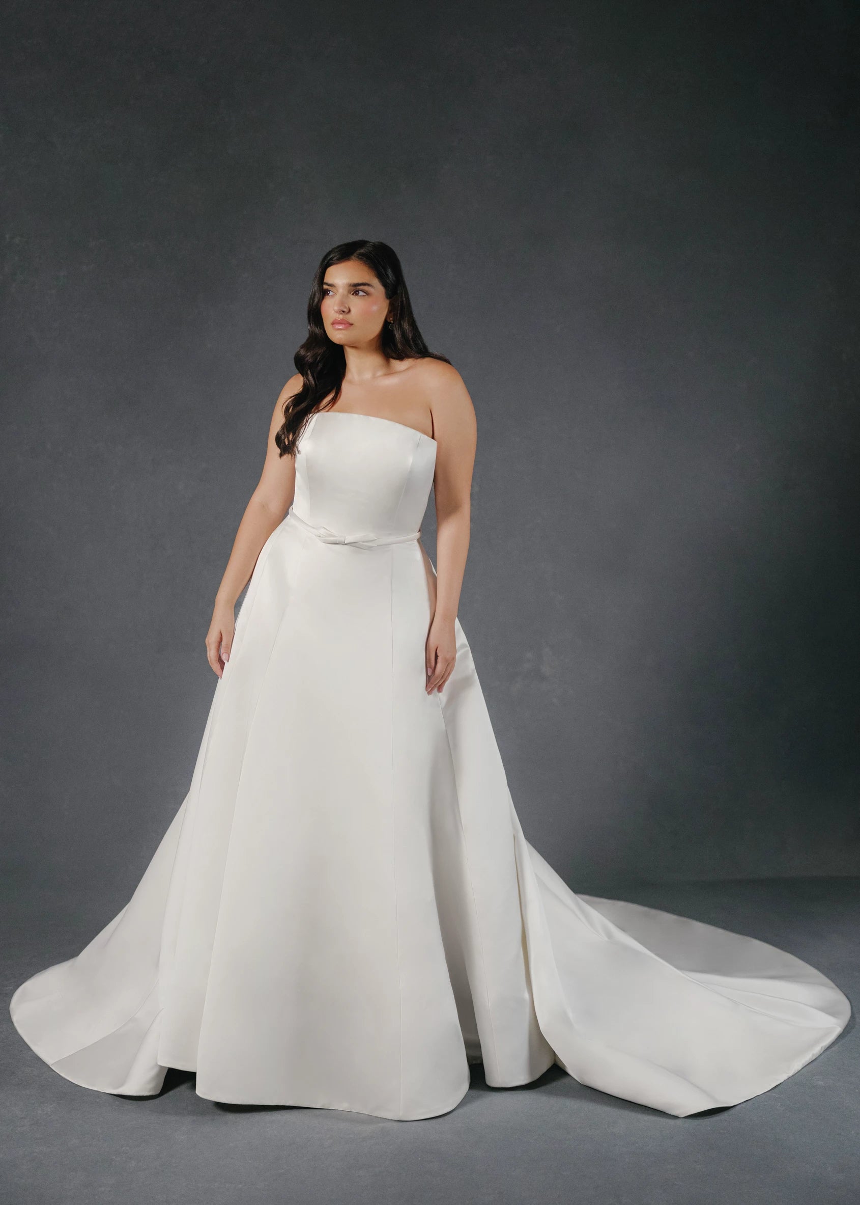 The Loyola gown is an arched strapless A-line gown of Faille-Back Satin with dramatic extended train and buttons to the hem in Silk White and Bright White. 