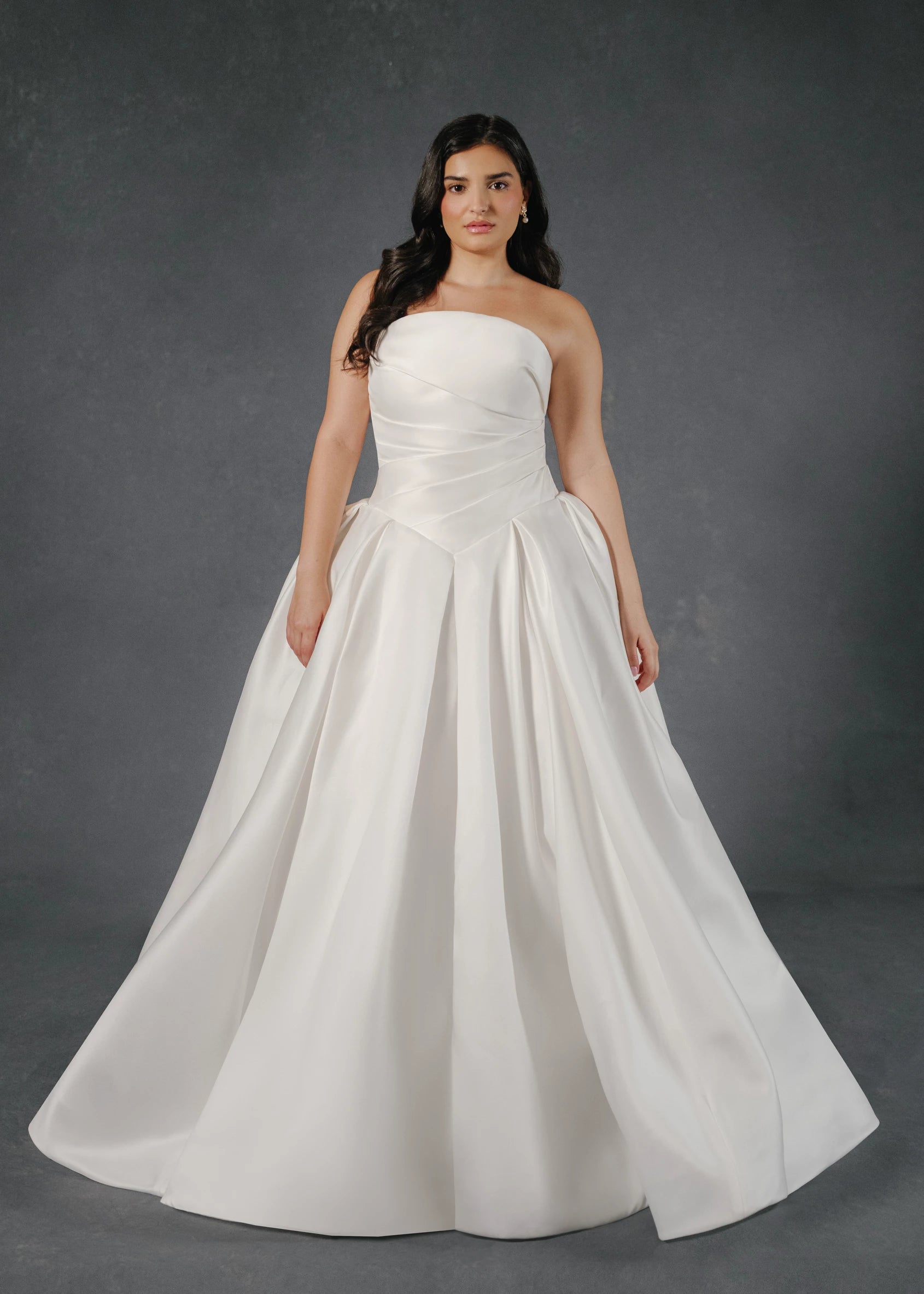 The Monarch gown is an arched strapless ballgown in Italian Lace Printed Matte Satin with asymmetrically draped bodice and basque waist on a dramatic box pleated skirt, with buttons to the hem in Pearl.