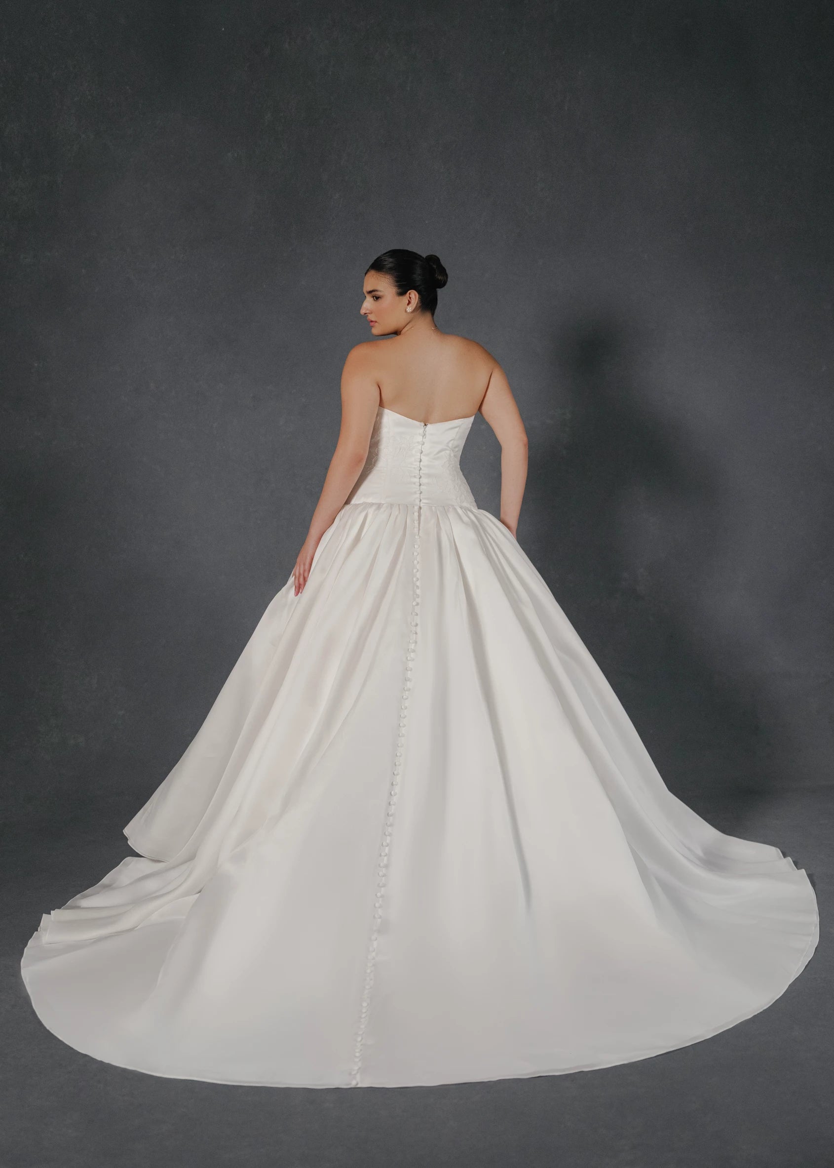 The Noblesse gown is a contour strapless drop waist ball gown of Silk Satin Organza with a draped neckline, delicate French Alençon lace appliqués, and a gathered skirt finished with buttons to the hem in Silk White.
