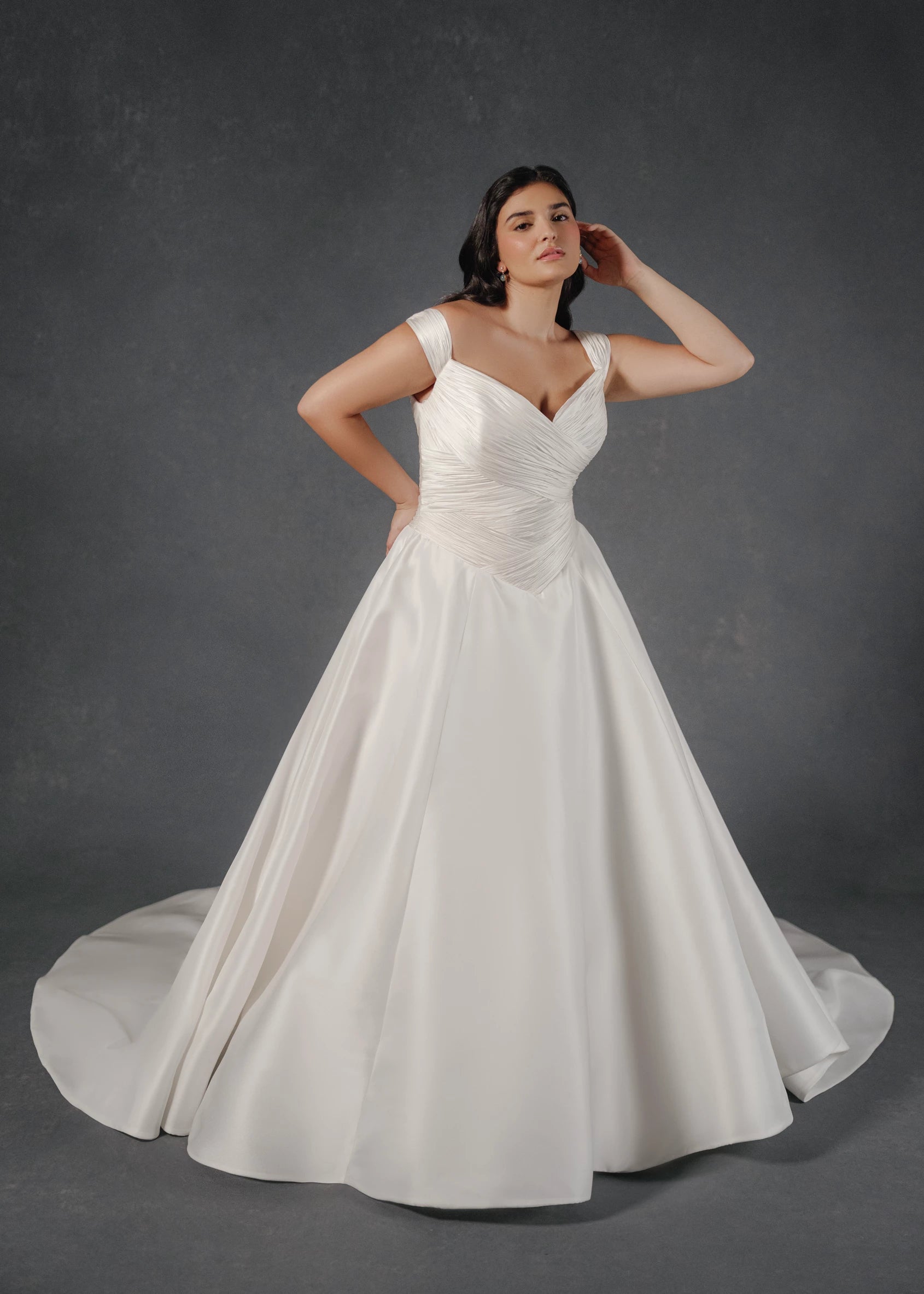 The Sabrina wedding dress is a timeless classic featuring a basque waist on a Silk White Satin Chiffon pleated, off-the-shoulder bodice with buttons to the waist and Kalika ballgown skirt.