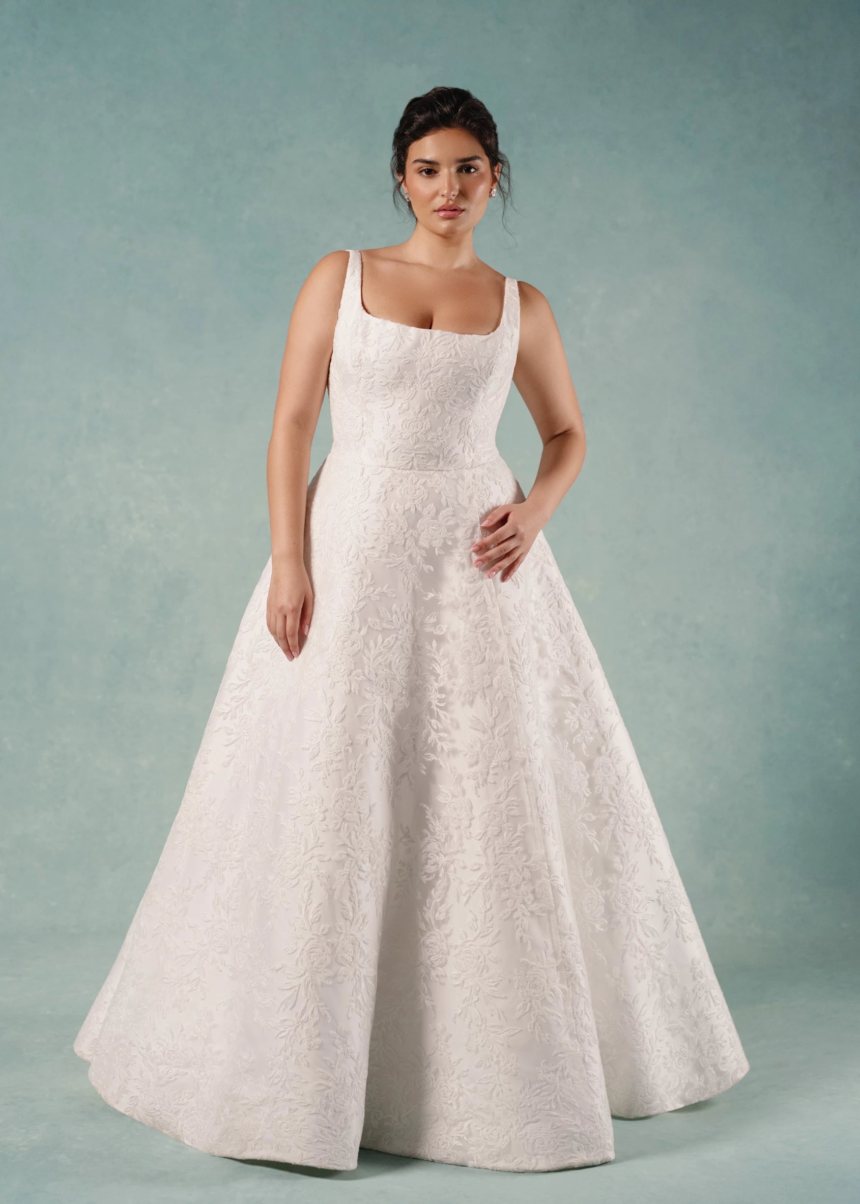 The Amelie gown is a scoop neck A-line gown in Soft Mikado with Thread-Sketched Floral Embroidery overlay and removeable Faille bow belt at the waist