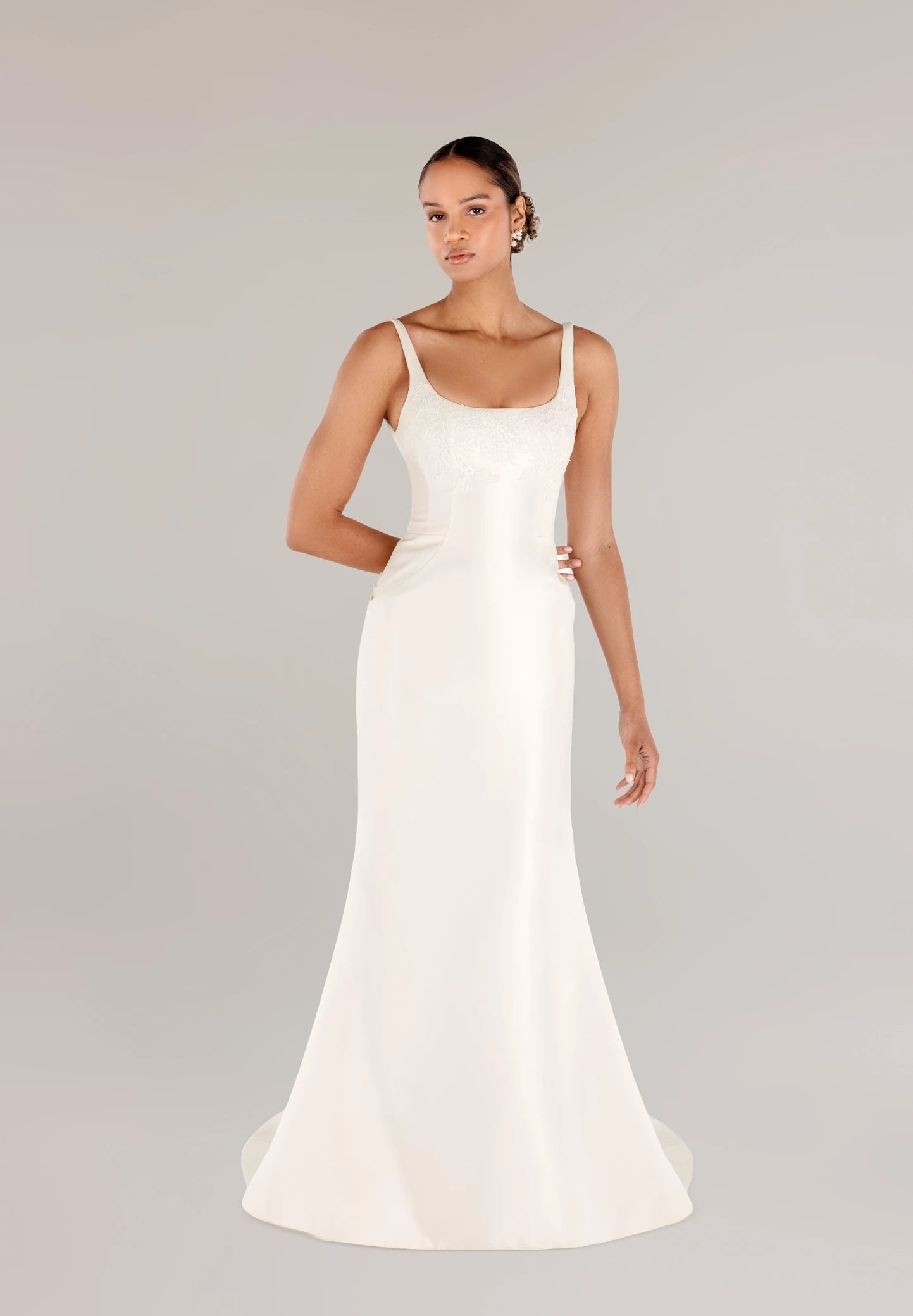 The Henrietta gown is a soft scoop neck trumpet gown of Italian Kalika with architectural seaming, featuring French Alençon lace framing the neckline in Pearl and Silk White.