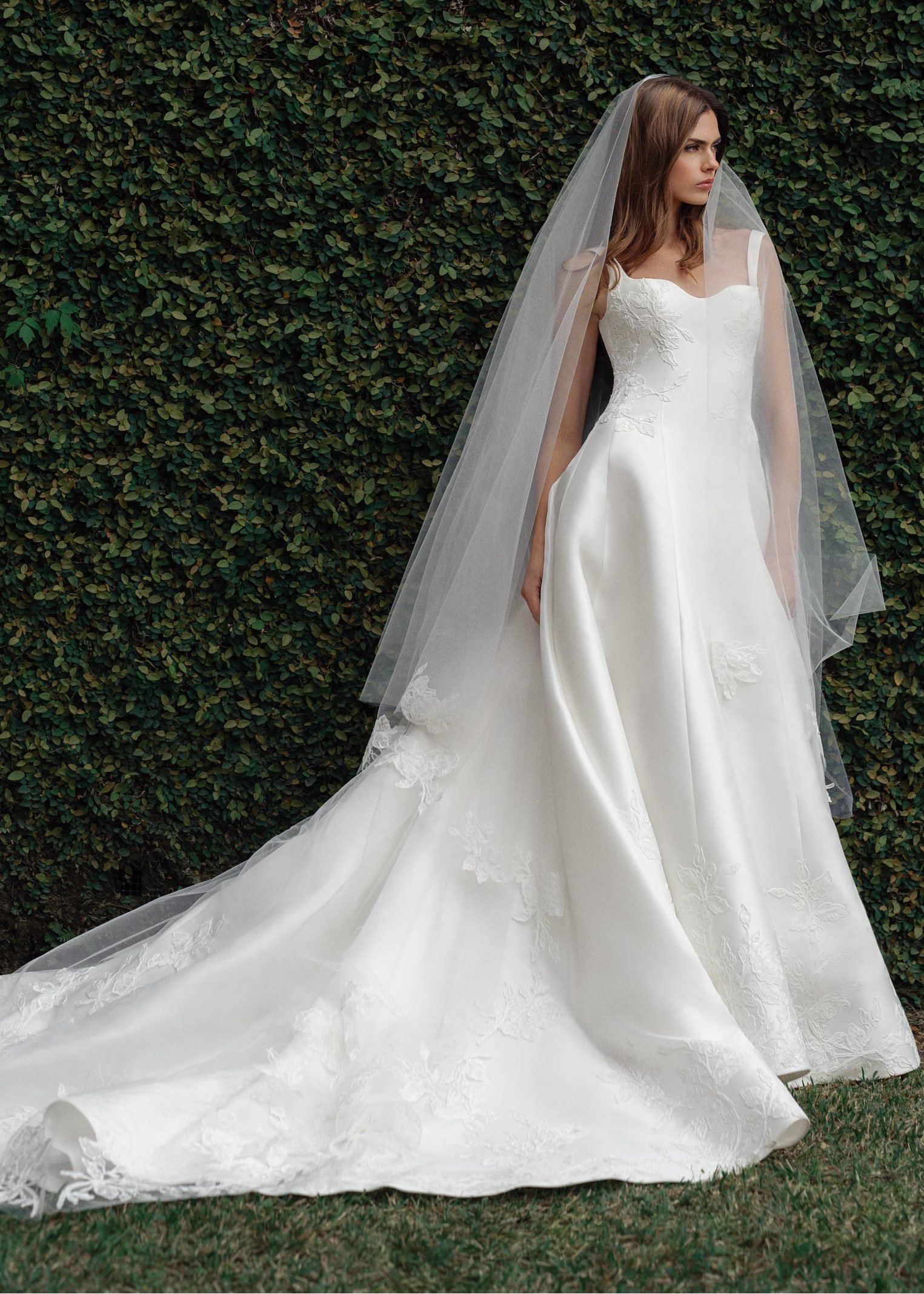 The King gown is a softly contoured sweetheart neckline A-line gown of Italian Kalika with Floral Vine Embroidered Lace appliqués framing the bodice and all around the skirt hem in Silk White.