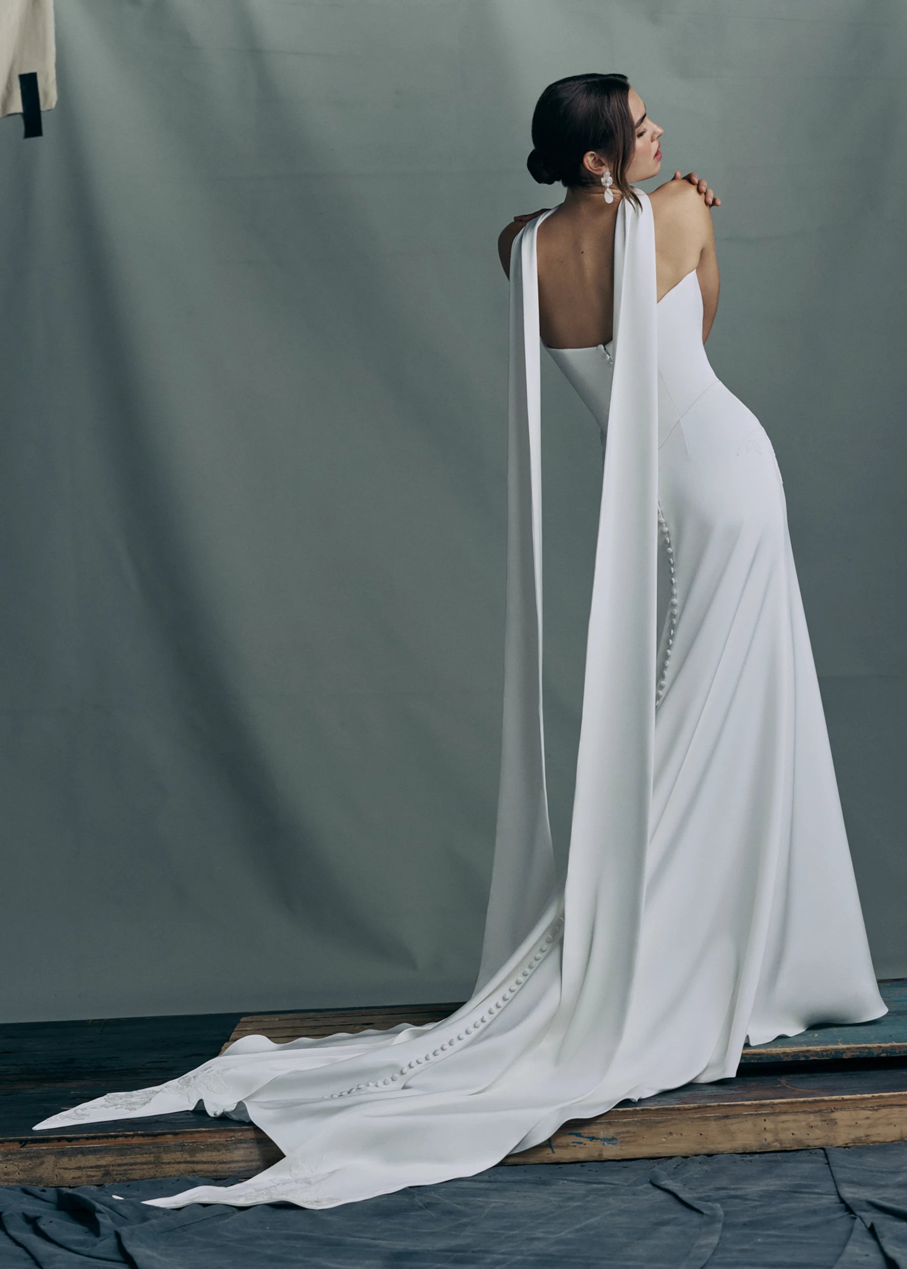 Back view of the Luminaire gown by Anne Barge, a strapless sweetheart gown in Crepe Back Satin, accented with Vine Embroidered Lace appliqués and pointed basque waist seam, with buttons to the hem in Silk White. Shown with the Luminaire Scarf, a neck scarf of Crepe Back Satin with Vine Embroidered Lace appliques at the edges.