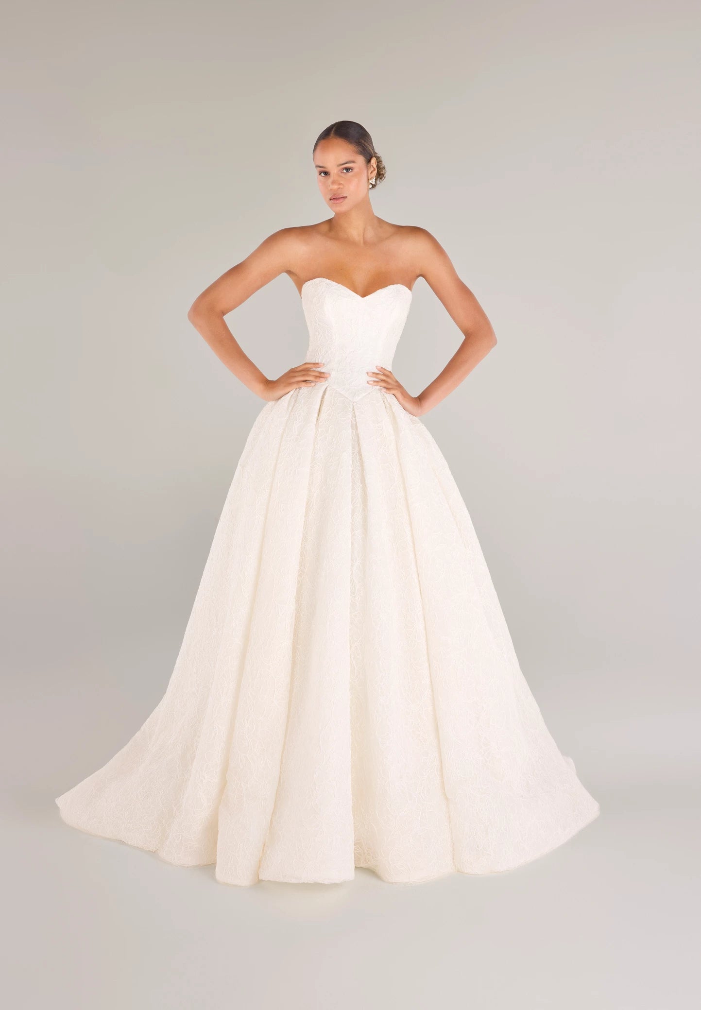 The Middleton gown is a strapless sweetheart ballgown in Corded Floral Lace with basque waist on a dramatic box pleated skirt, with buttons to the end of the zipper in Silk White.