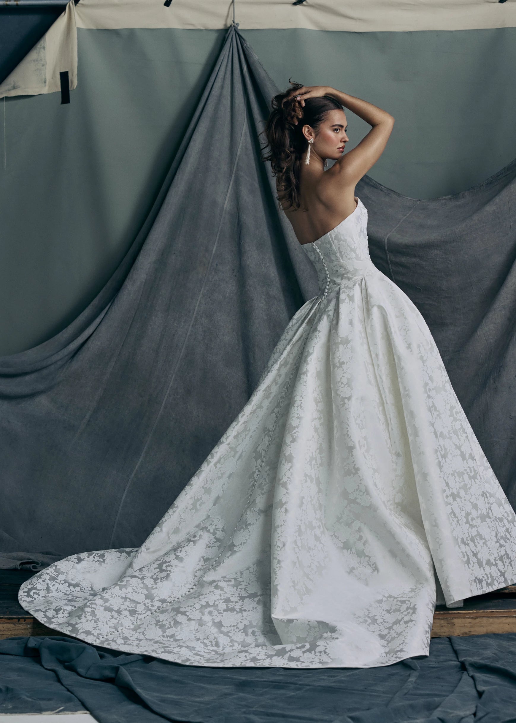 The back view of the Monarch gown by Anne Barge is an arched strapless ballgown in Italian Lace Printed Matte Satin with asymmetrically draped bodice and basque waist on a dramatic box pleated skirt, with buttons to the hem in Pearl.