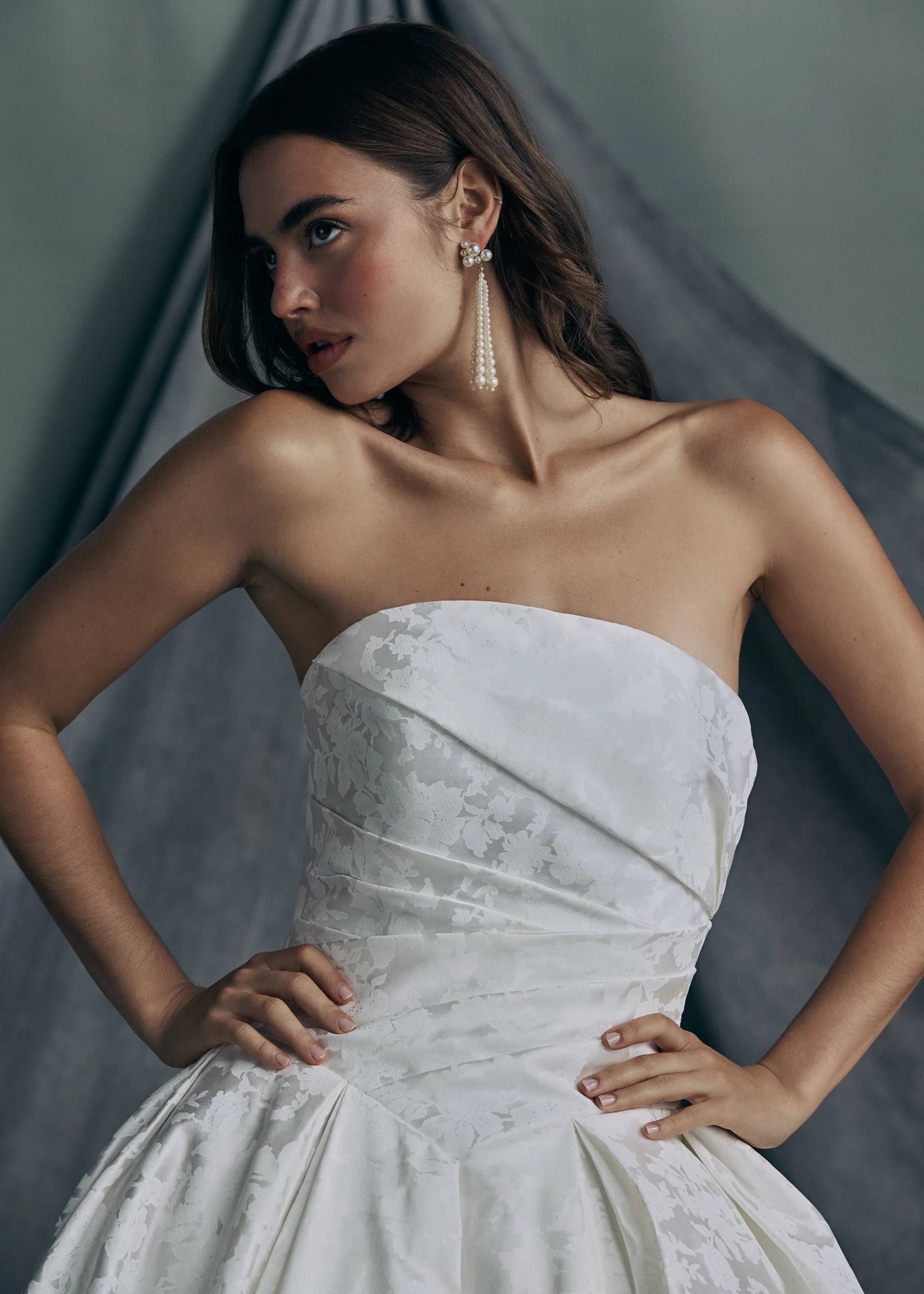 The Monarch gown by Anne Barge is an arched strapless ballgown in Italian Lace Printed Matte Satin with asymmetrically draped bodice and basque waist on a dramatic box pleated skirt, with buttons to the hem in Pearl.