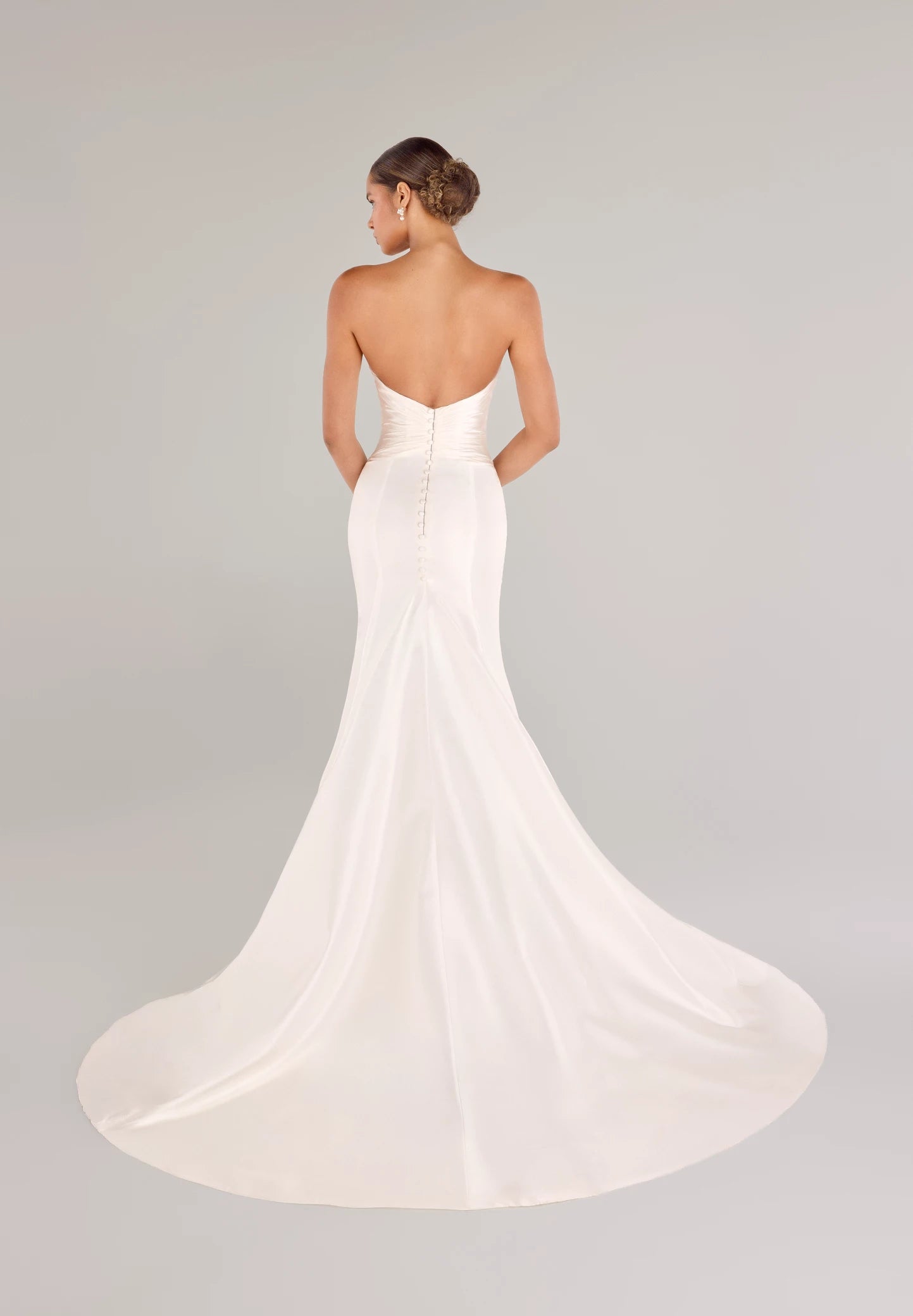 The Montagu gown is a trumpet gown of Italian Kalika with a narrow plunging V-neckline bodice, intricately pleated in Silk Satin Chiffon, and buttons to the top of the godet in Silk White. 