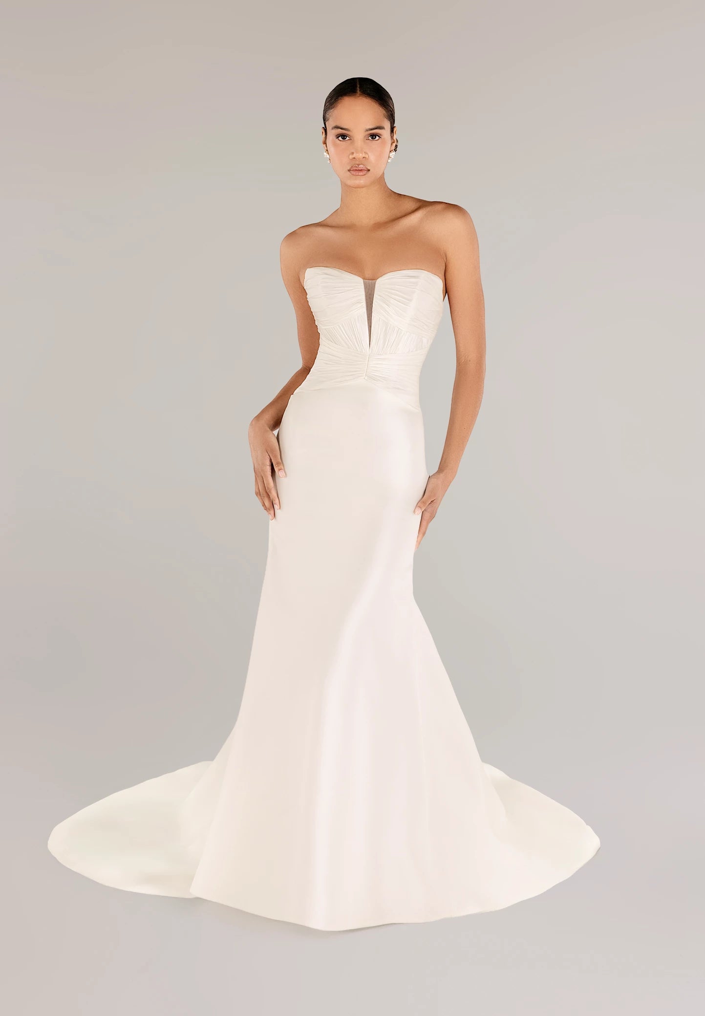 The Montagu gown is a trumpet gown of Italian Kalika with a narrow plunging V-neckline bodice, intricately pleated in Silk Satin Chiffon, and buttons to the top of the godet in Silk White. 