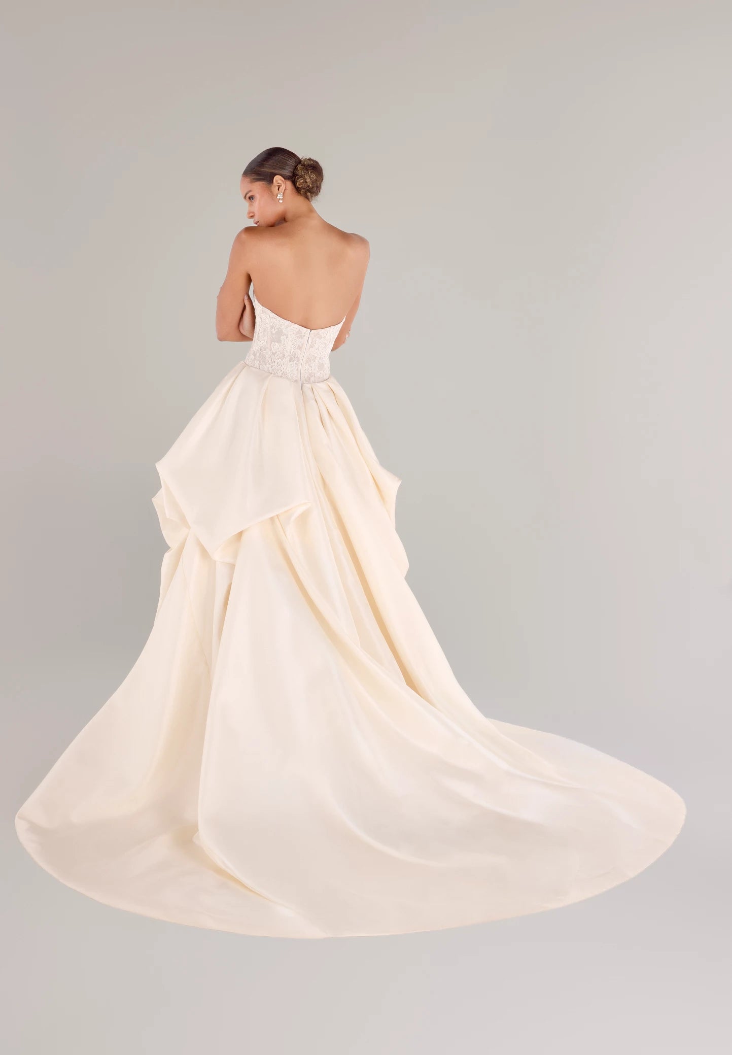 The Wentworth gown is a strapless drop waist corset bodice of French Alençon and Chantilly laces with an Italian Kalika ballgown skirt featuring sculptural origami-style pick-ups and asymmetric waterfall draping in Pearl and Silk White.