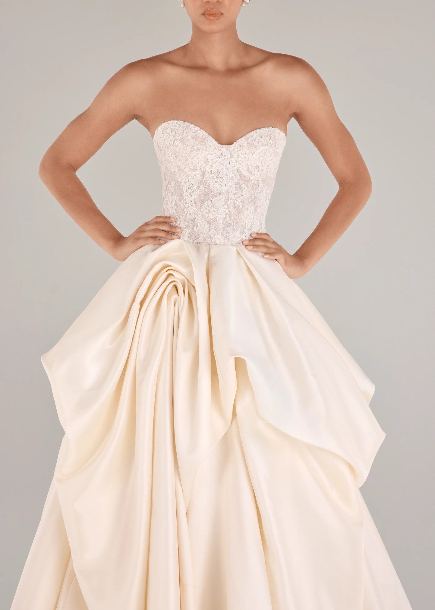 The Wentworth gown is a strapless drop waist corset bodice of French Alençon and Chantilly laces with an Italian Kalika ballgown skirt featuring sculptural origami-style pick-ups and asymmetric waterfall draping in Pearl and Silk White. 