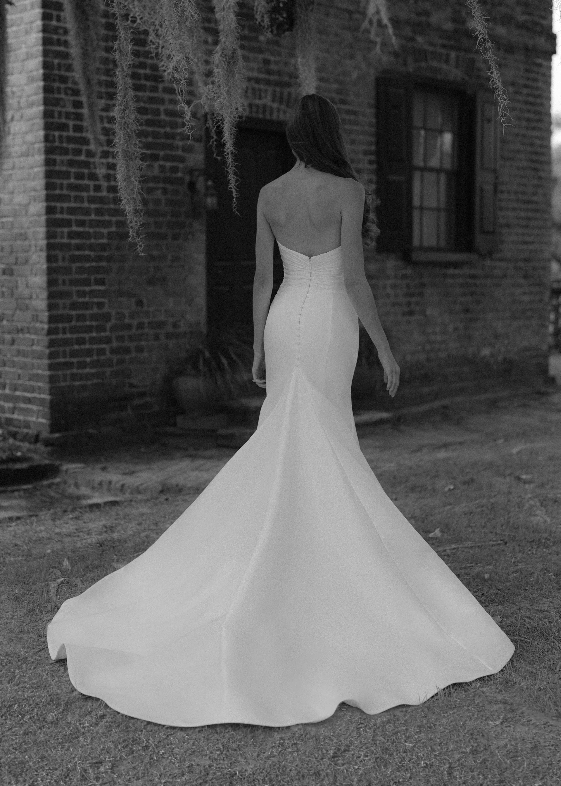 The Montagu gown is a trumpet gown of Italian Kalika with a narrow plunging V-neckline bodice, intricately pleated in Silk Satin Chiffon, and buttons to the top of the godet in Silk White. 