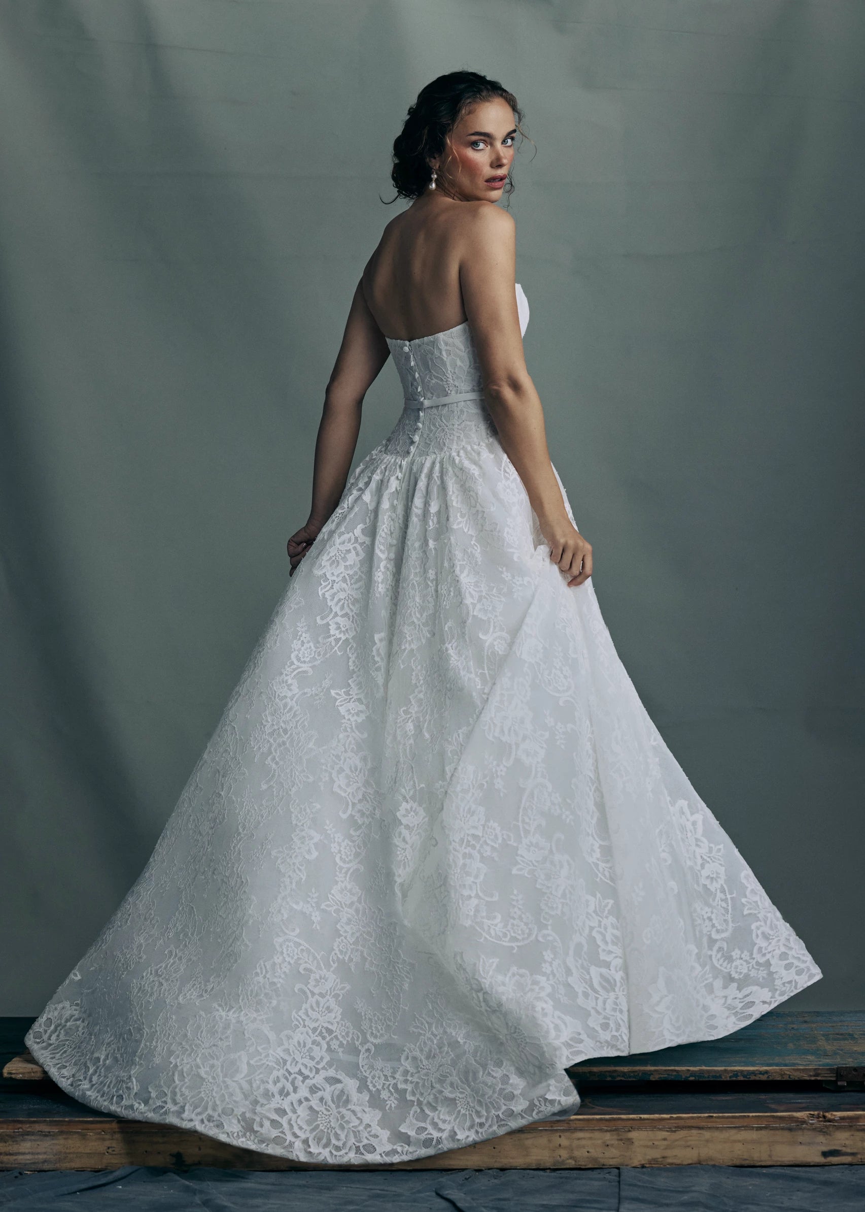 Back view of the The Albertine gown by Anne Barge, a sculpted sweetheart strapless ballgown in Chantilly lace, featuring a ziggurat dropped waist and buttons to the hem in Silk White.