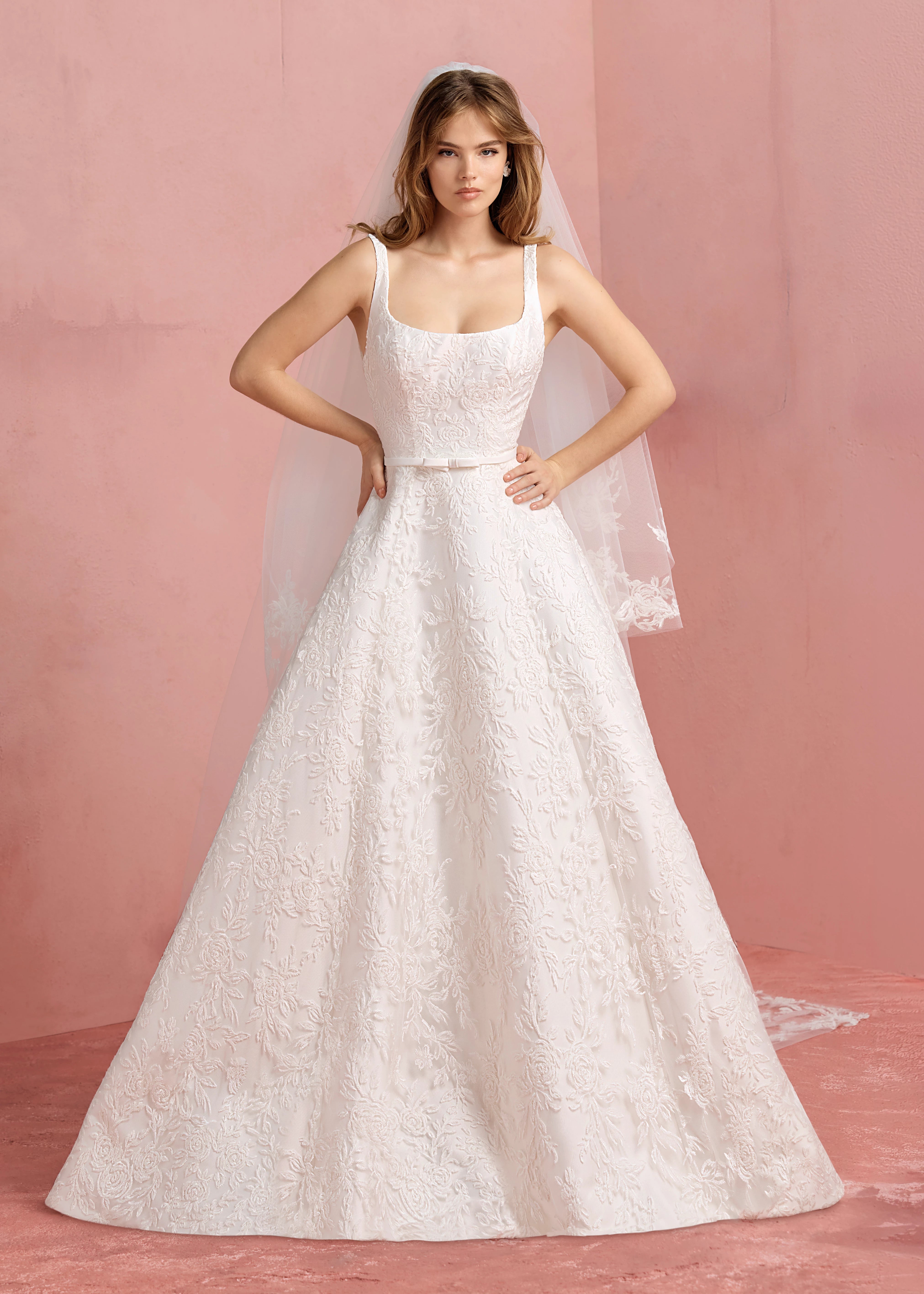 The Amelie gown is a scoop neck A-line gown in Soft Mikado with Thread-Sketched Floral Embroidery overlay, buttons to the hem and faille bow belt in Pearl.