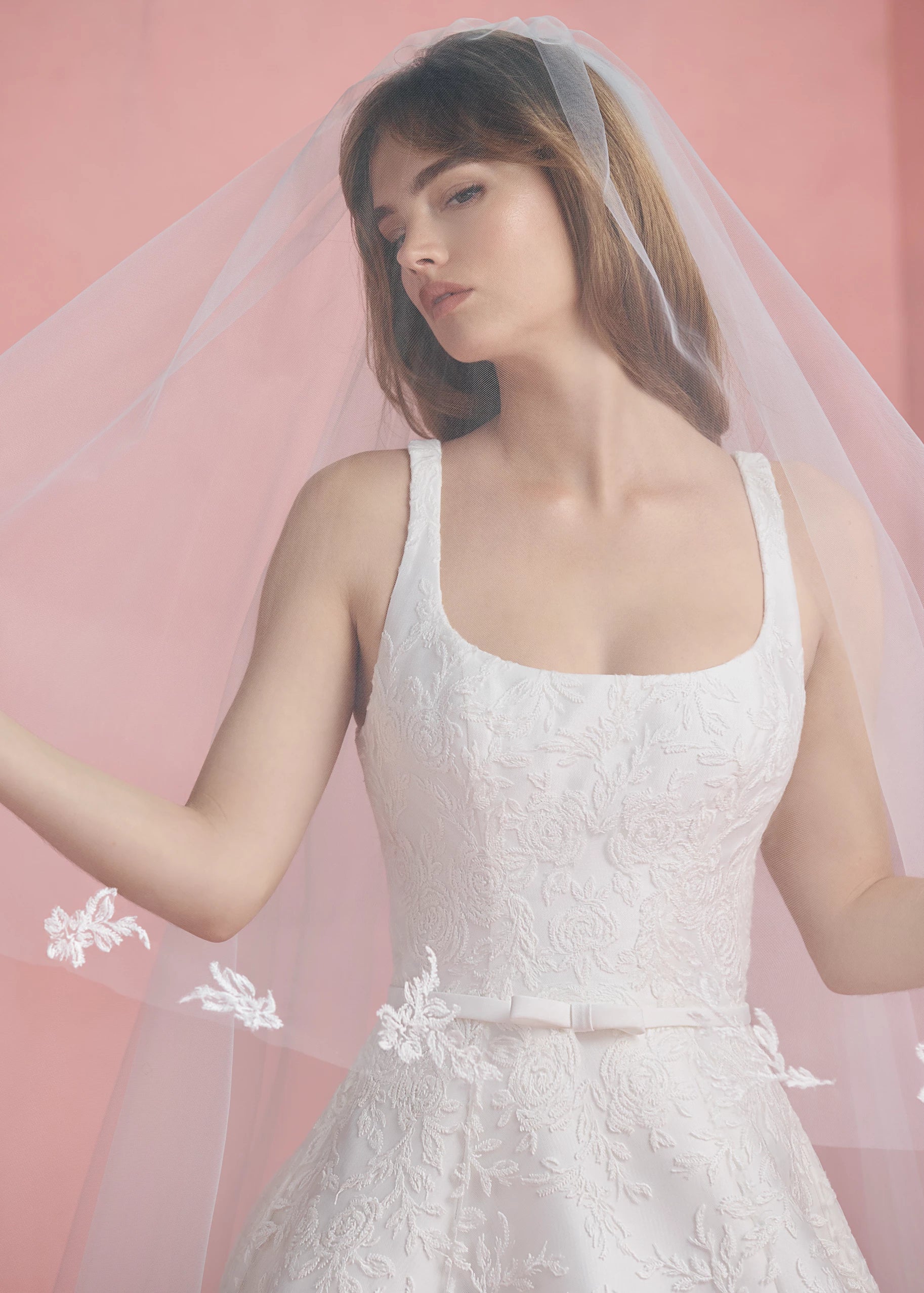 The Amelie gown is a scoop neck A-line gown in Soft Mikado with Thread-Sketched Floral Embroidery overlay, buttons to the hem and faille bow belt in Pearl.