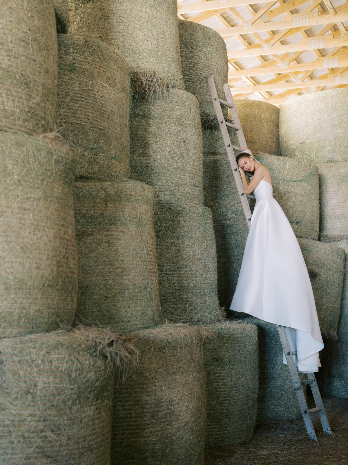 The Avelina gown is a strapless ballgown of Soft Mikado featuring a draped bodice and box pleated skirt with pockets, finished with buttons to the hem in Pearl and Bright White. 