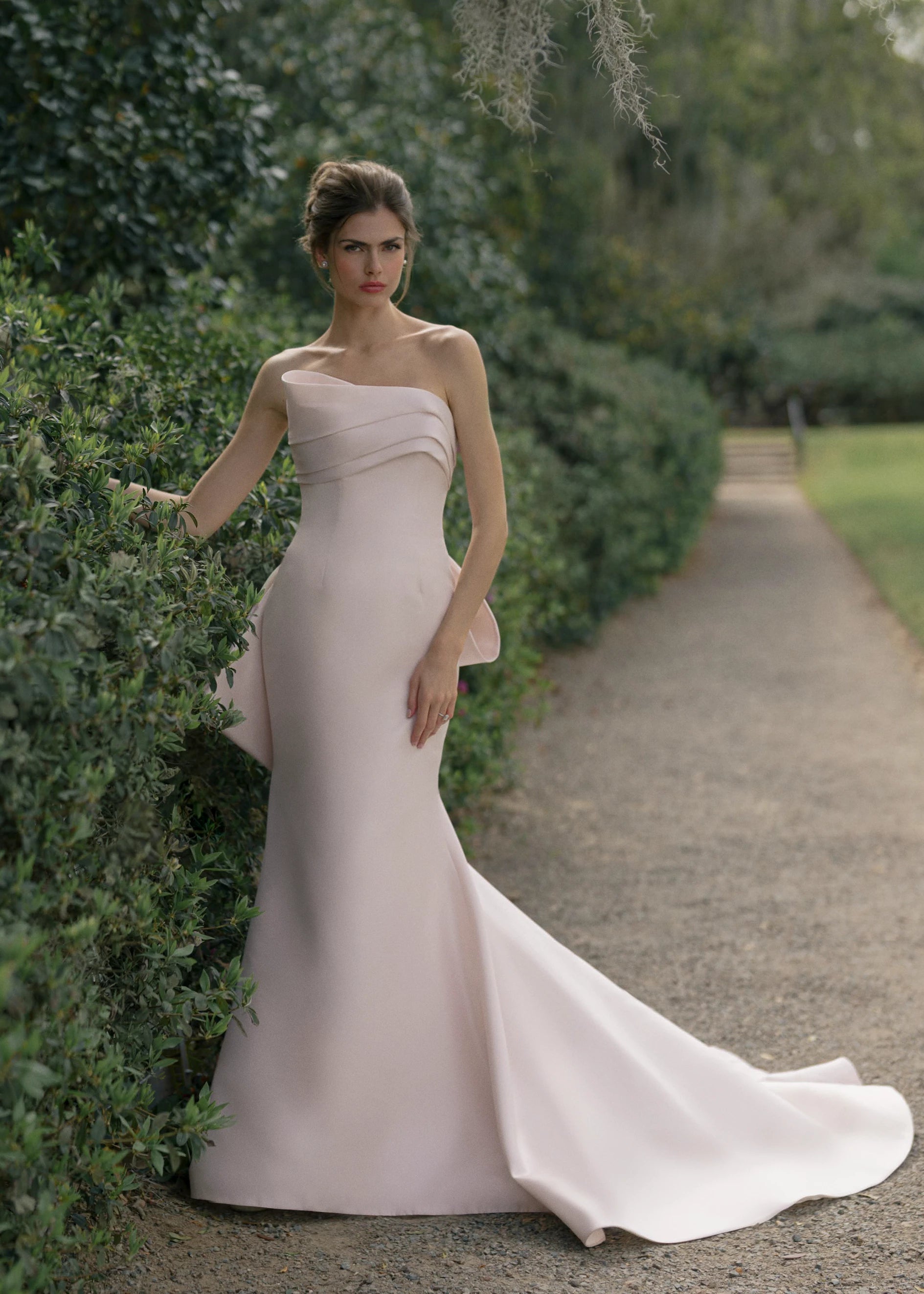The Daniels gown is a fit and flare gown of Kalika featuring an asymmetrically draped bodice cuff, oversized sculptural bow, and buttons to the hem.