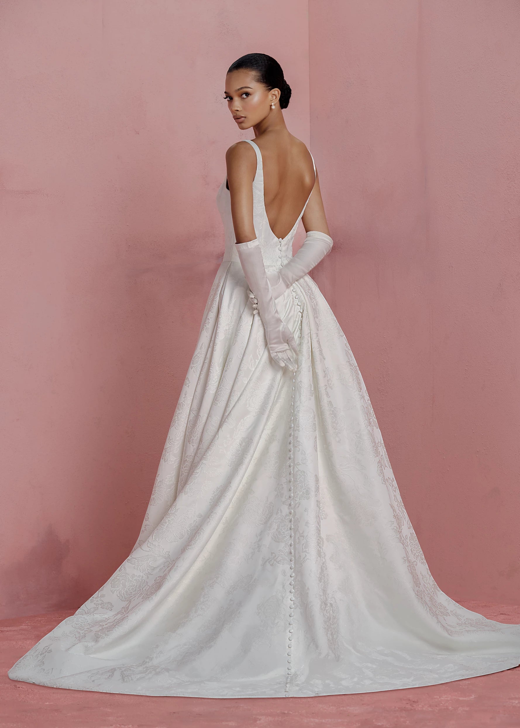 Back view of the Elodie gown by Anne Barge is a square neck column gown in Embossed Jacquard with low back and buttons to the hem, featuring box-pleated attached overskirt in Pearl.