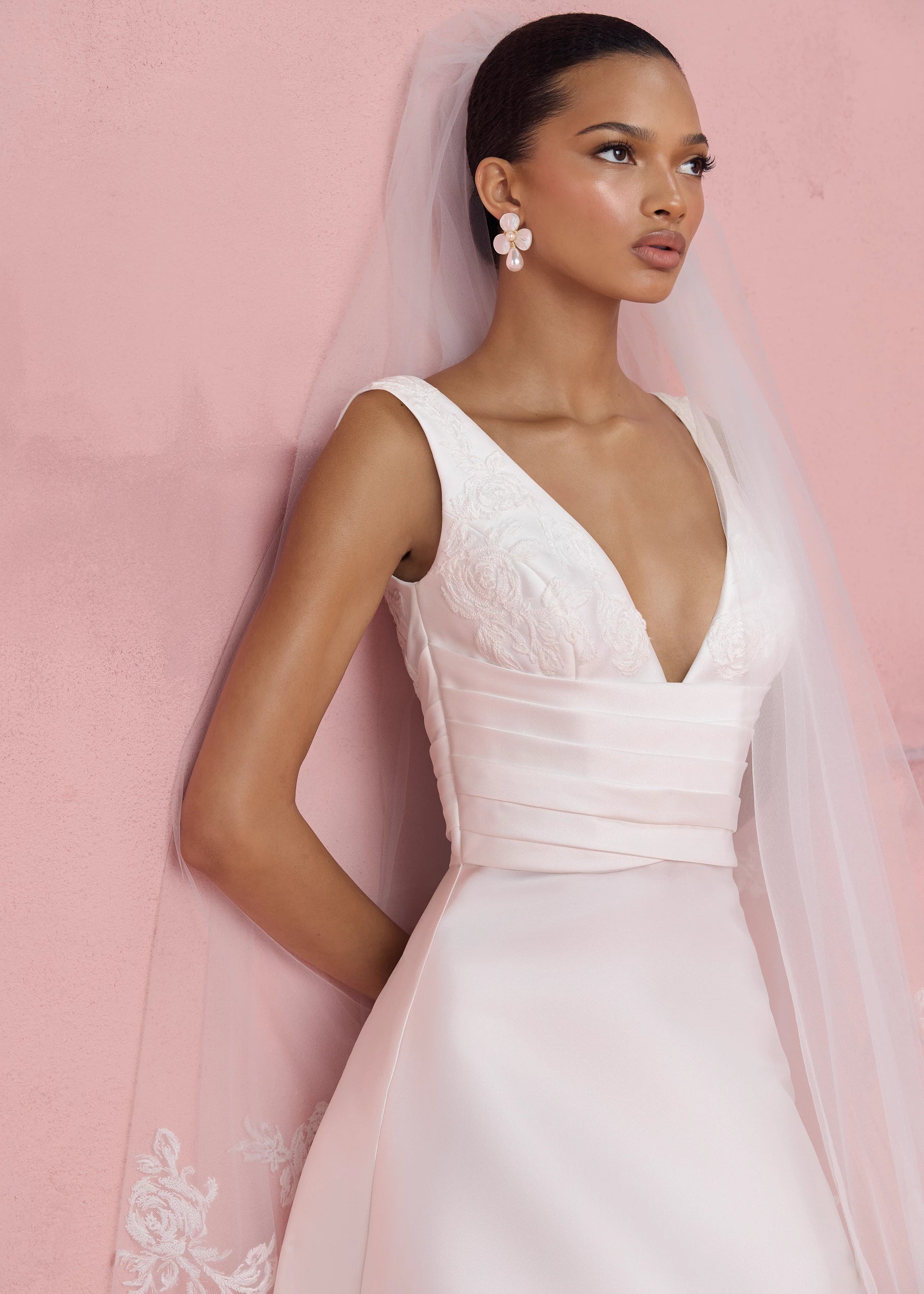 The Joelle gown is a soft Mikado modified A-line gown with plunging V-neckline accented with Thread-Sketched Floral Embroidered Appliques, pleated cummerbund waist, and buttons to the hem in Pearl.