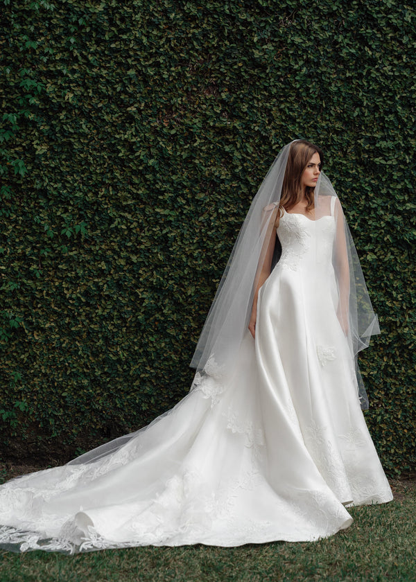 The King gown is a softly contoured sweetheart neckline A-line gown of Italian Kalika with Floral Vine Embroidered Lace appliqués framing the bodice and all around the skirt hem in Silk White.