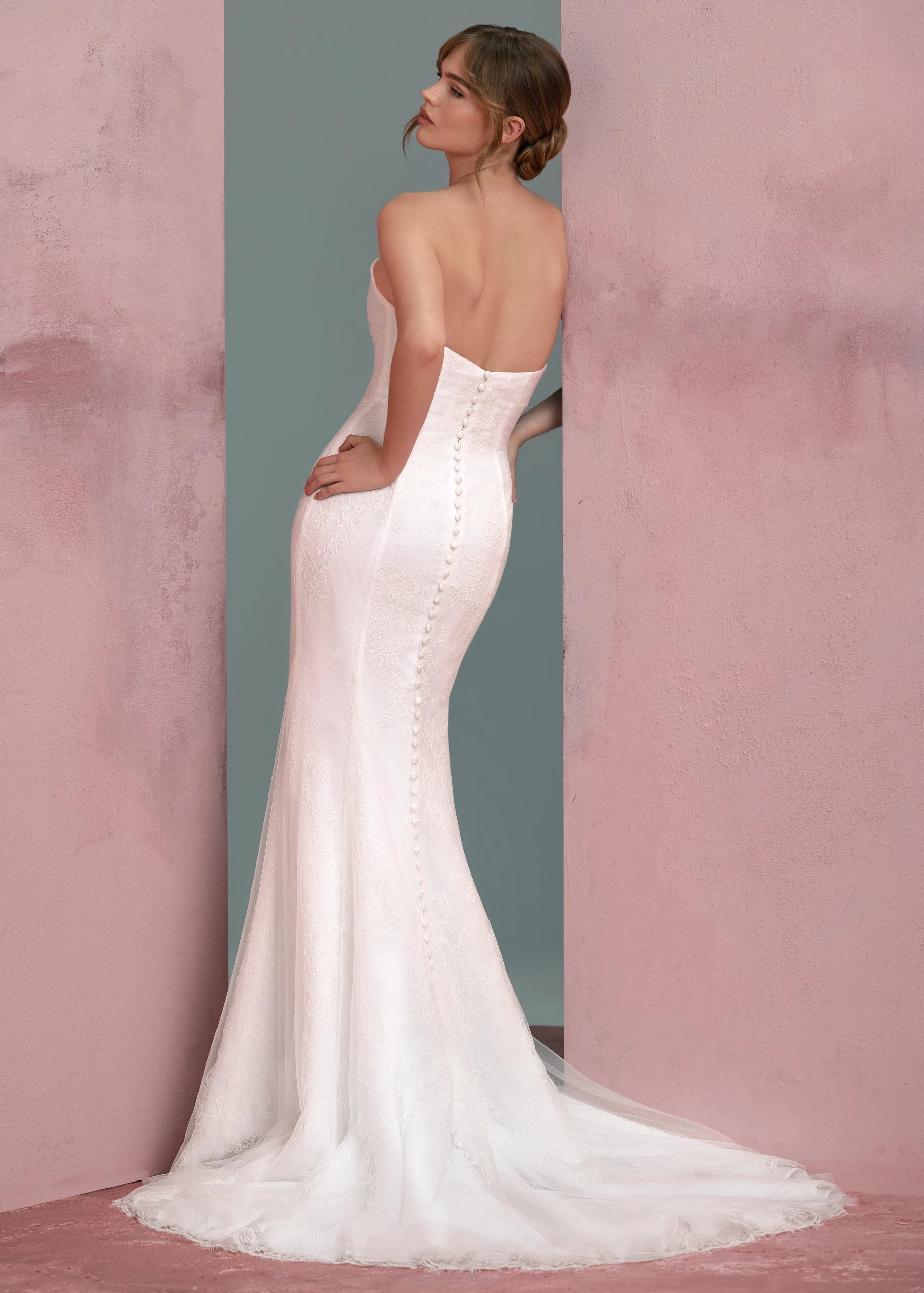 Back view of The Lucienne gown by Anne Barge is a cat-eye strapless column gown of Corded Lace with pleated Illusion Tulle overlay, featuring buttons to the hem in Silk White.