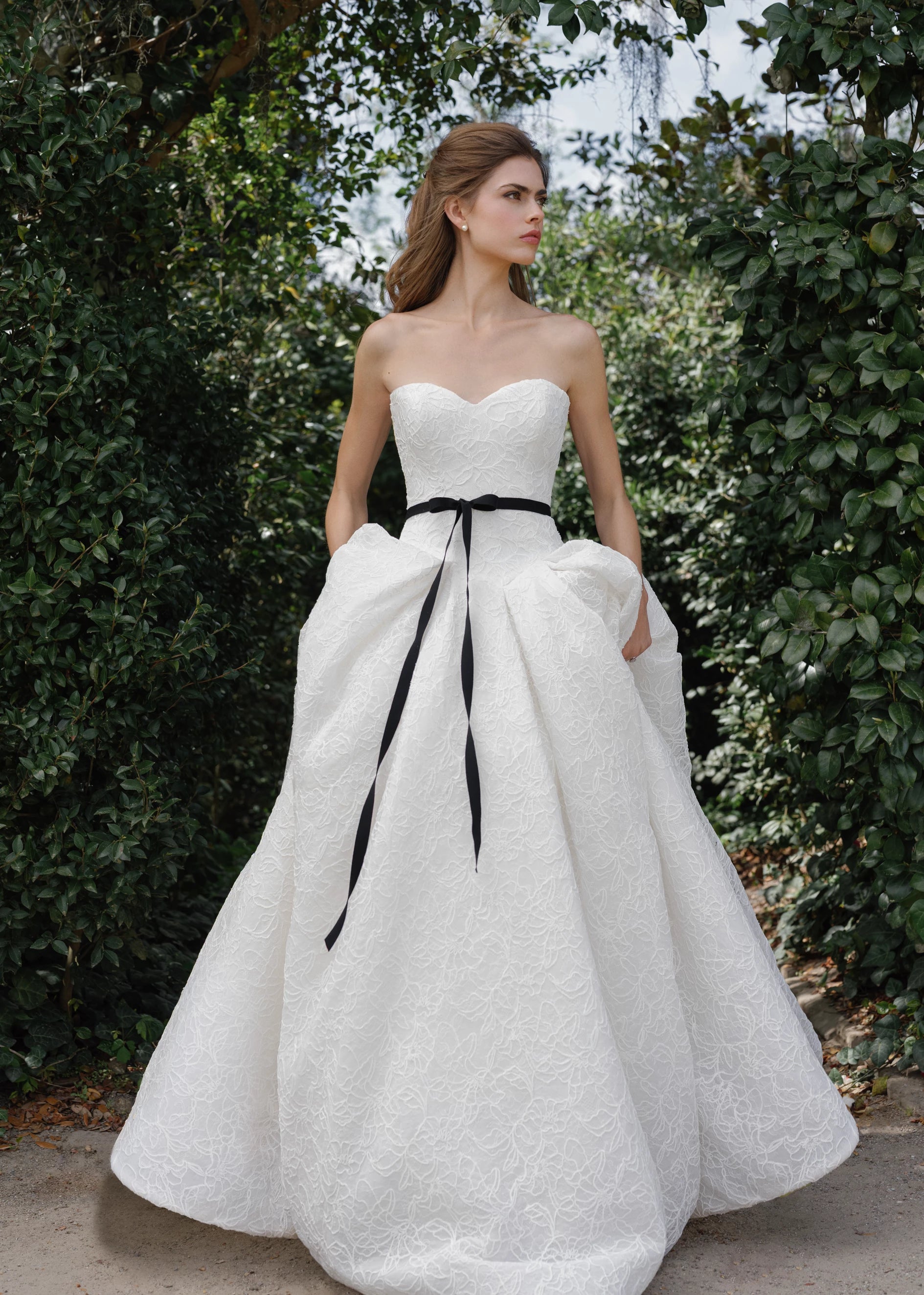 The Middleton gown is a strapless sweetheart ballgown in Corded Floral Lace with basque waist on a dramatic box pleated skirt, with buttons to the end of the zipper in Silk White. 