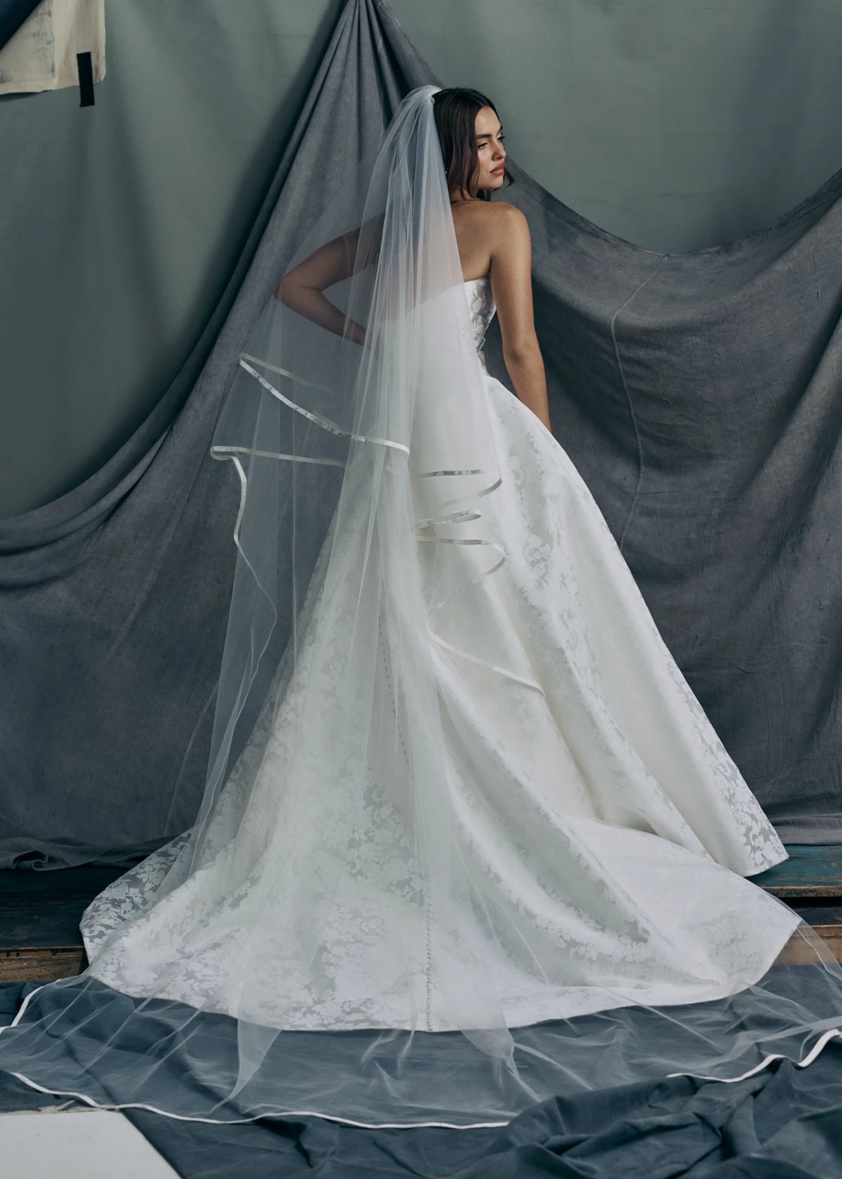 The back view of the Monarch gown by Anne Barge is an arched strapless ballgown in Italian Lace Printed Matte Satin with asymmetrically draped bodice and basque waist on a dramatic box pleated skirt, with buttons to the hem in Pearl.