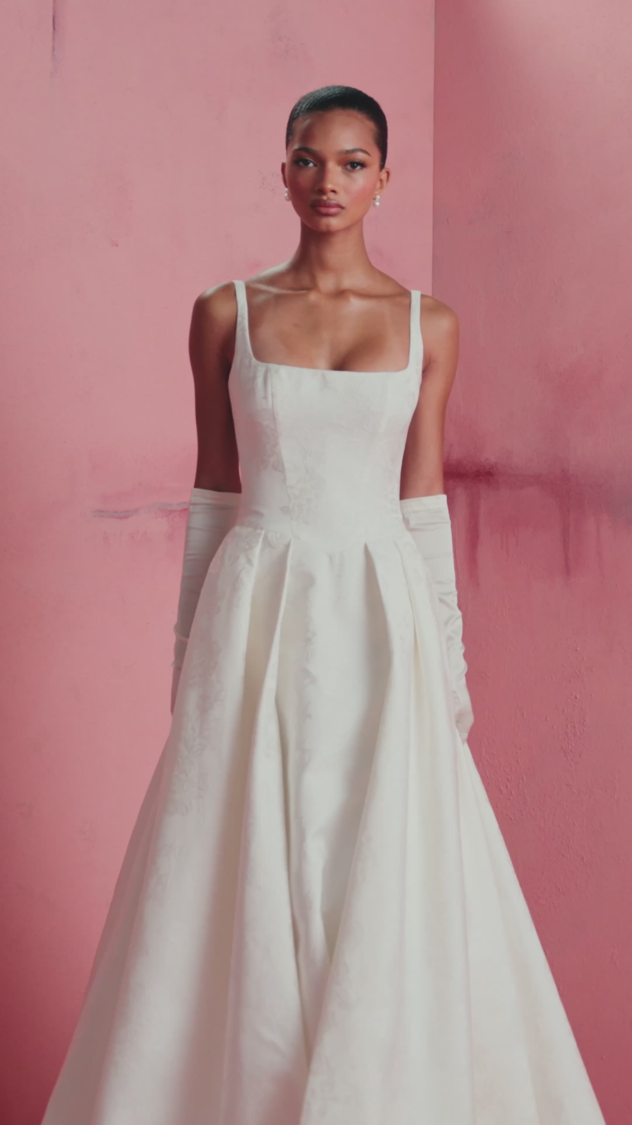 The Elodie gown by Anne Barge is a square neck column gown in Embossed Jacquard with low back and buttons to the hem, featuring box-pleated attached overskirt in Pearl.