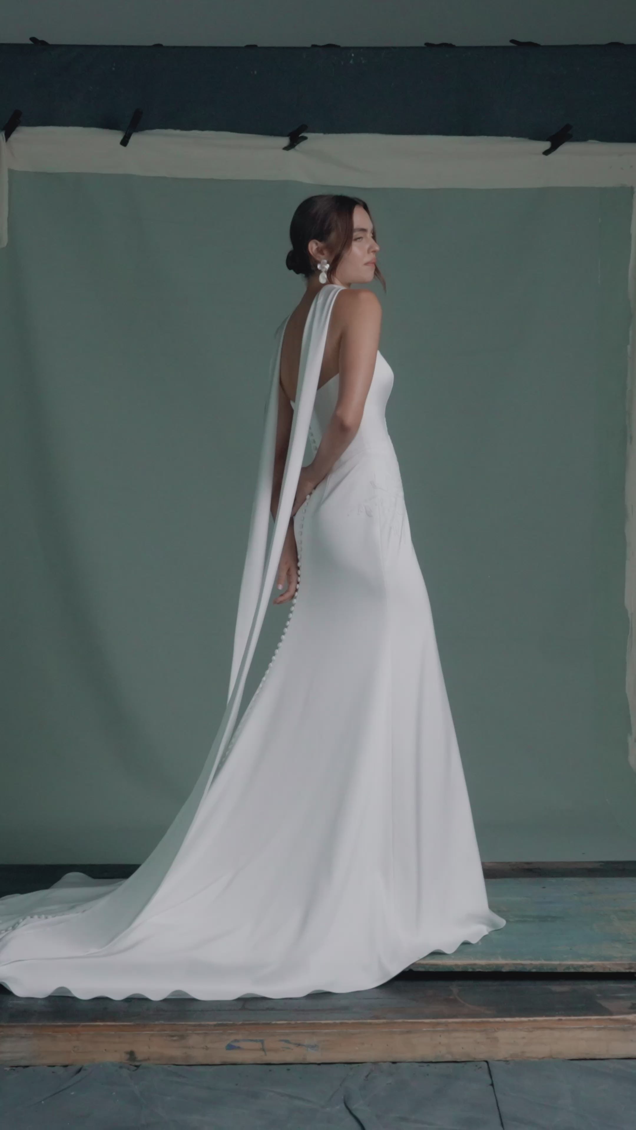 The Luminaire gown by Anne Barrge is a strapless sweetheart gown in Crepe Back Satin, accented with Vine Embroidered Lace appliqués and pointed basque waist seam, with buttons to the hem in Silk White. Shown with the Luminaire Scarf, a neck scarf of Crepe Back Satin with Vine Embroidered Lace appliques at the edges.