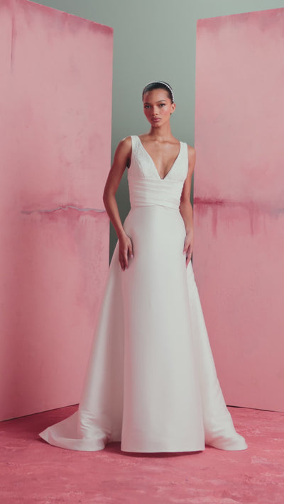 The Joelle gown by Anne Barge is a soft Mikado modified A-line gown with plunging V-neckline accented with Thread-Sketched Floral Embroidered Appliques, pleated cummerbund waist, and buttons to the hem in Pearl.