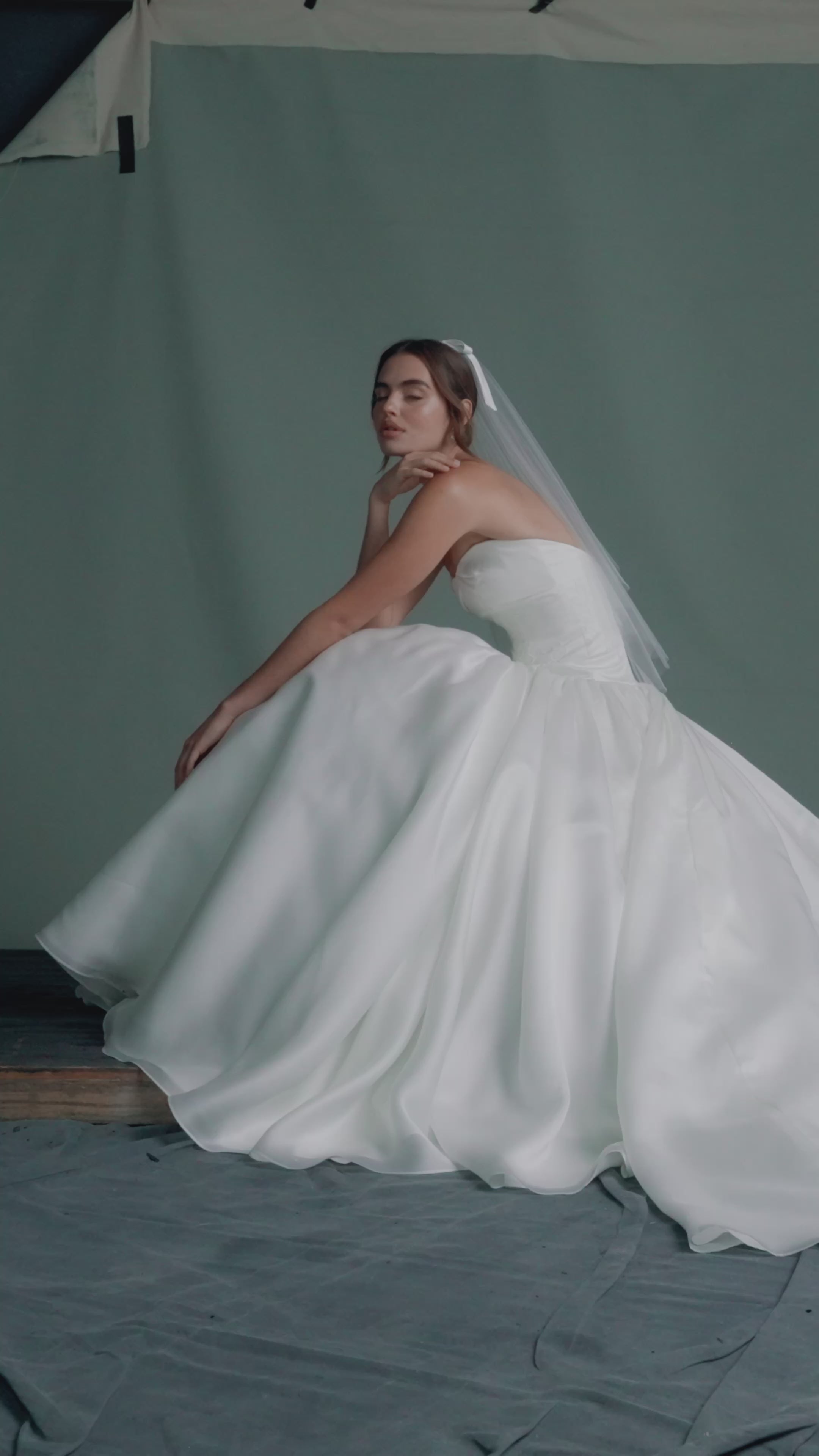 The Noblesse gown by Anne Barge is a contour strapless drop waist ball gown of Silk Satin Organza with a draped neckline, delicate French Alençon lace appliqués, and a gathered skirt finished with buttons to the hem in Silk White.
Paired with the Noblesse Top, an Illusion tulle long sleeve mockneck topper appliquéd with French Alençon lace.