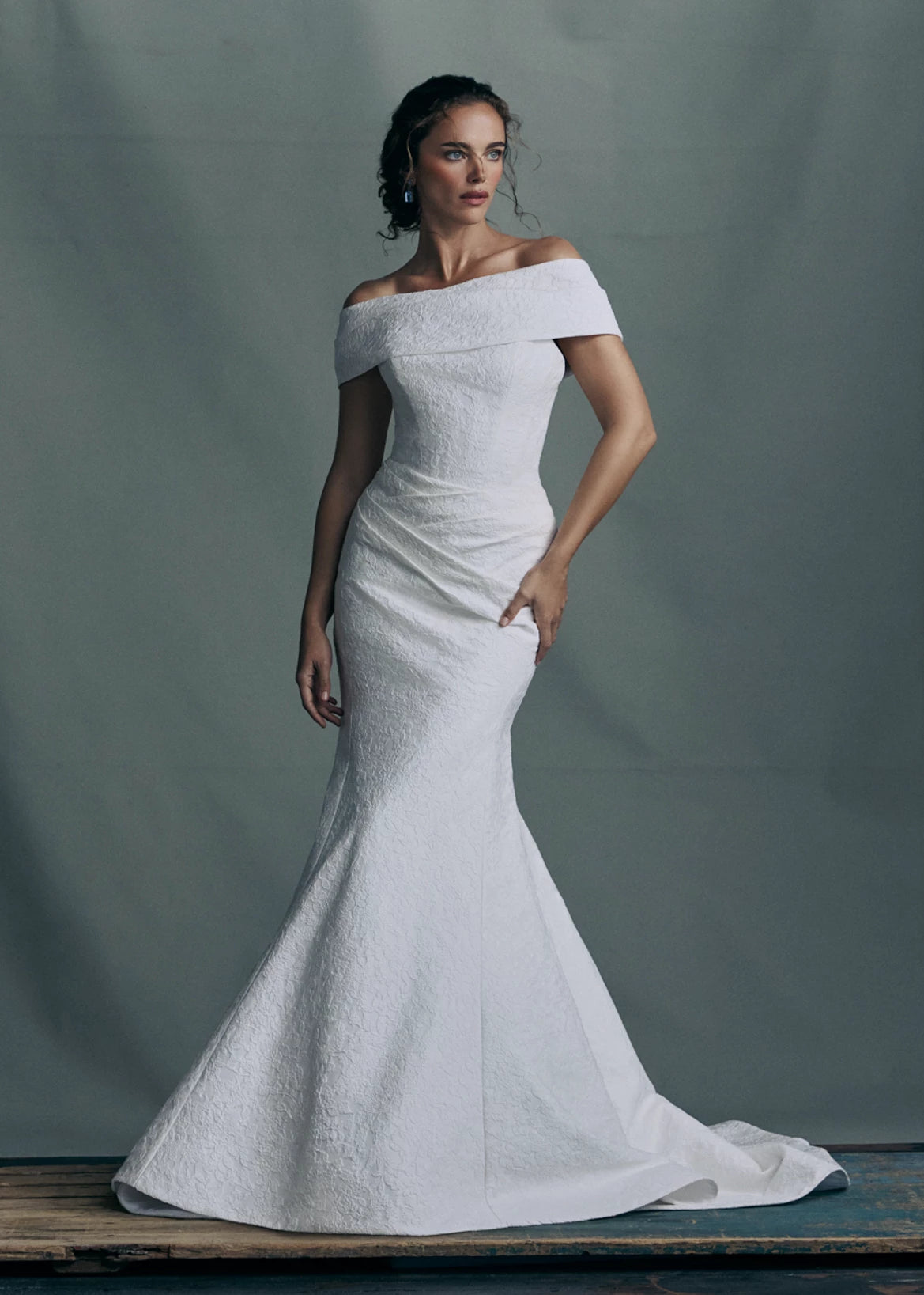 The Sera gown by Anne Barge is a strapless rounded cat-eye fit and flare gown in Spanish Lacework Jacquard, accented by diagonal draping across the skirt and buttons to the hem in Silk White. The Sera gown includes the Sera Shawl, a detachable off-the-shoulder shawl in Lacework Jacquard.