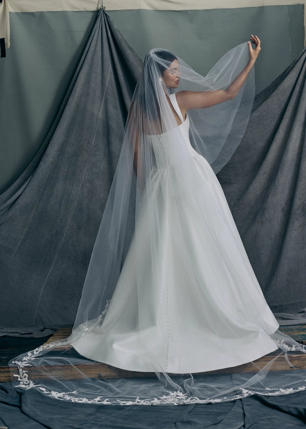 The Verité Veil is a Cathedral length veil featuring delicate hand-embroidered beaded floral vines accented with bow motifs and simple fold over blusher.